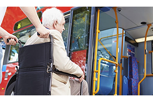 An elderly man in a wheelchair helped onto a transportation vehicle