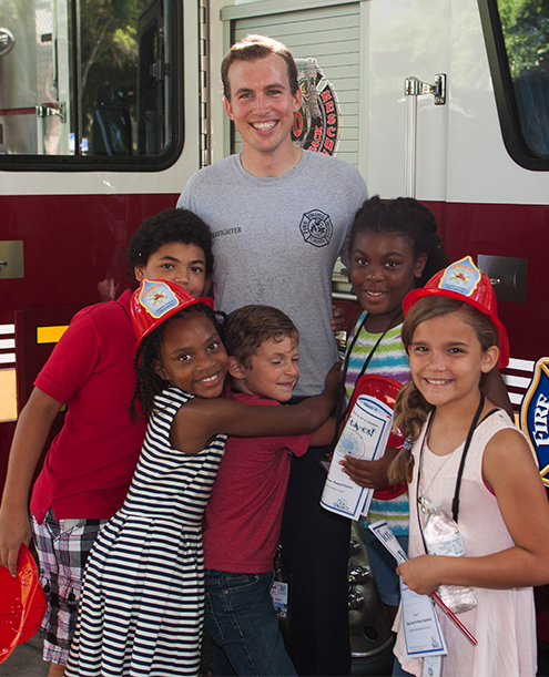 Niños abrazados a un bombero en frente de un camión de bomberos